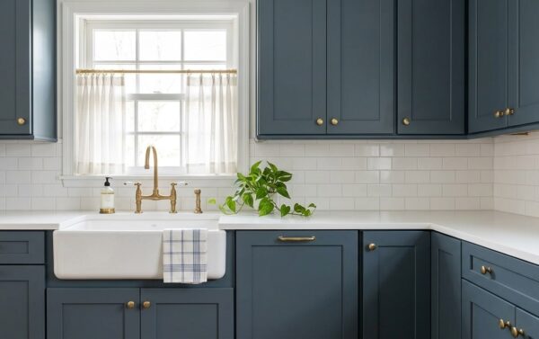 A kitchen with blue cabinets, white countertops, and brass faucet.